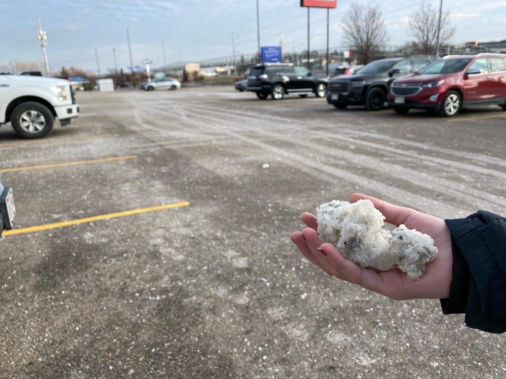 picture of a woman's hand holding chunks of salt against the background of an oversalted parking lot